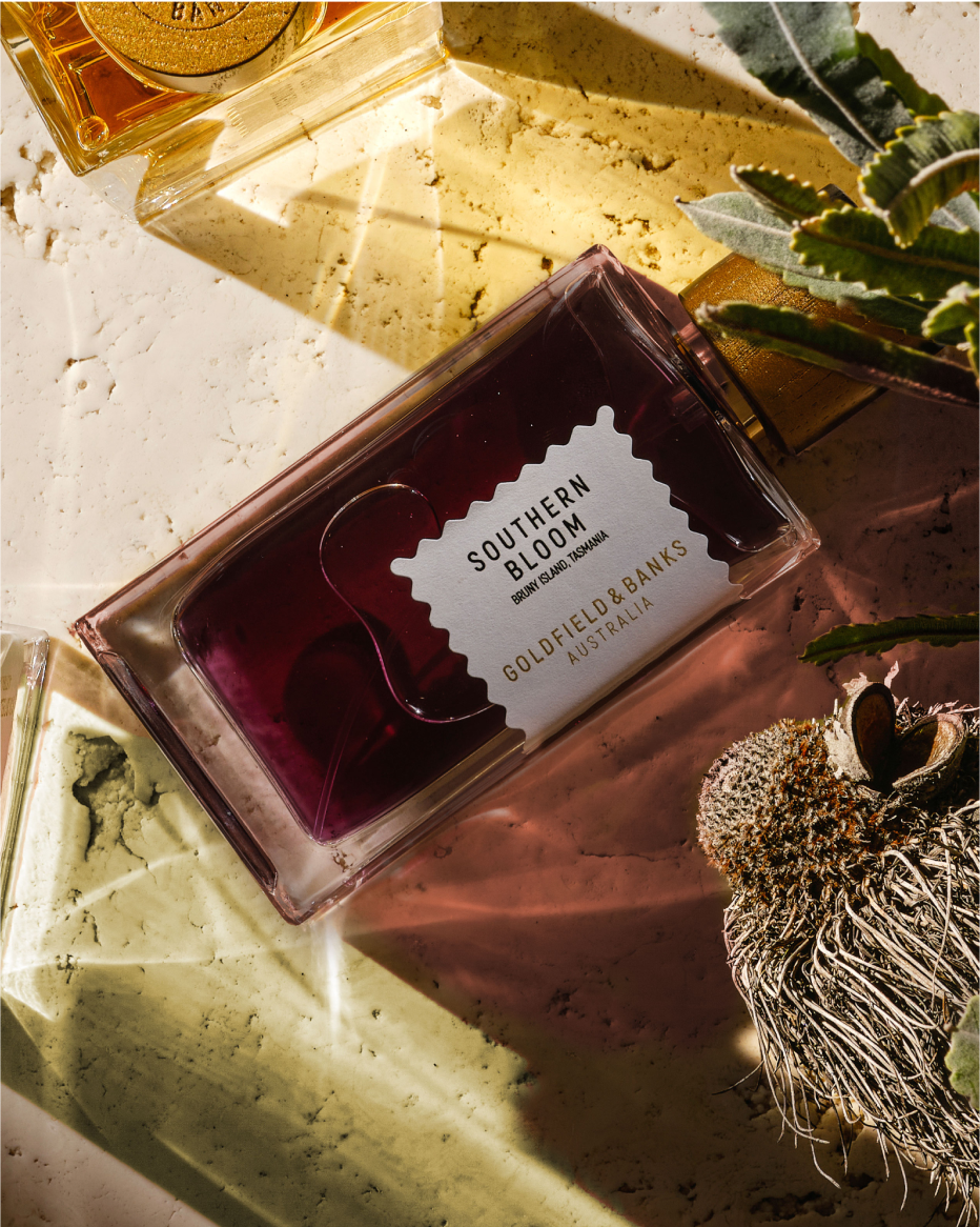 Goldfield & Banks Southern Bloom perfume bottle with deep red liquid, styled with native Australian botanicals and warm natural light, showcasing a luxurious floral fragrance composition.
